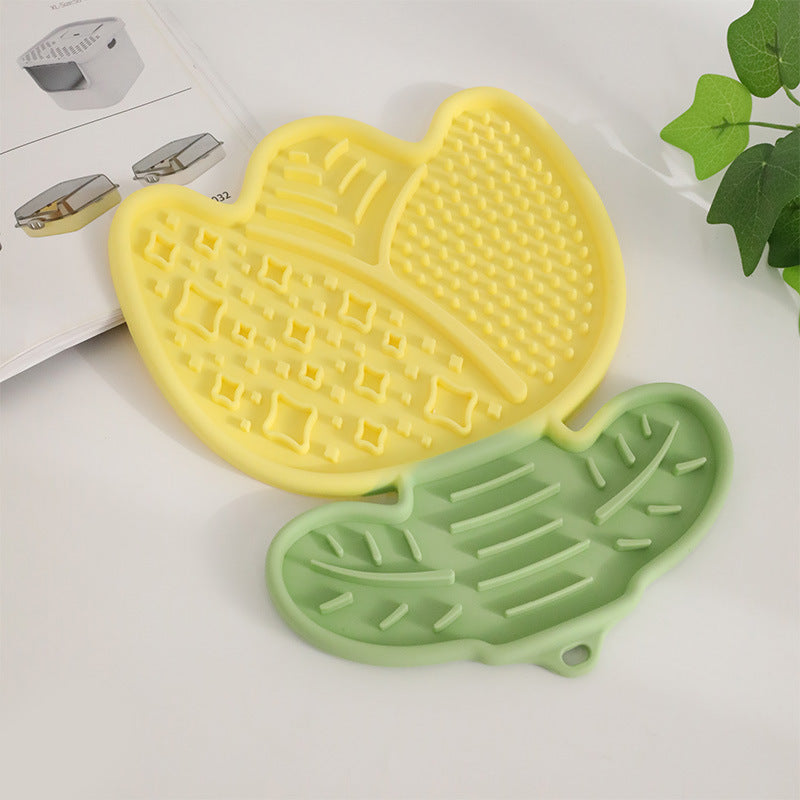 Yellow and green silicone pet mat on a white surface with a plant in the background
